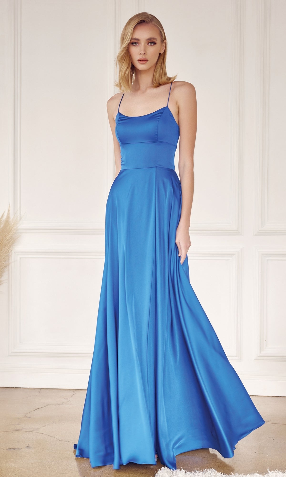 A woman stands indoors wearing the Strappy-Back Simple Long A-Line Prom Dress 278—a bright blue satin, sleeveless formal dress with thin straps. She has blonde hair and a neutral expression.